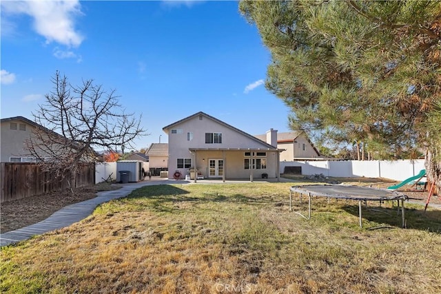 back of property featuring a trampoline, a patio area, a lawn, and a storage unit