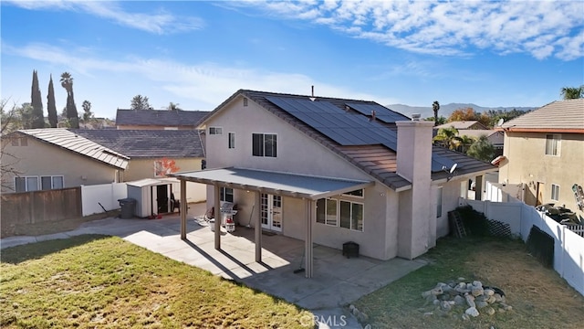 back of house featuring a storage shed, french doors, a patio, a lawn, and solar panels