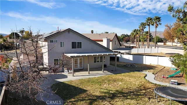 rear view of house with a trampoline, a patio area, french doors, and a lawn