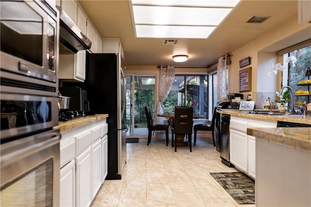 kitchen with ventilation hood, stainless steel microwave, white cabinetry, and sink