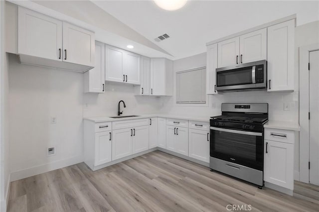 kitchen featuring white cabinetry, sink, vaulted ceiling, appliances with stainless steel finishes, and light wood-type flooring