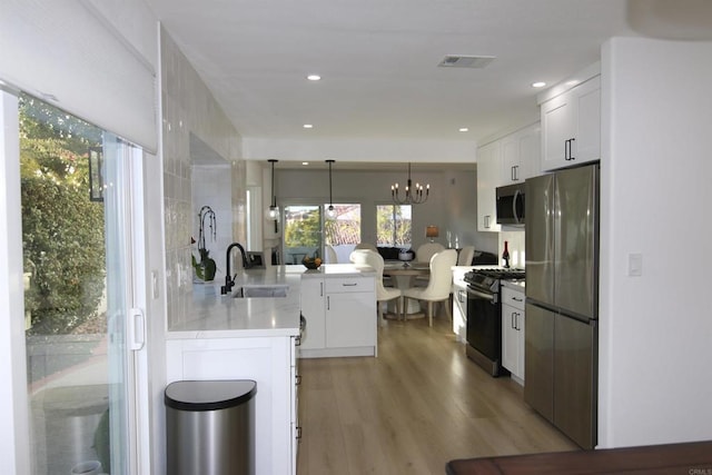 kitchen featuring sink, hanging light fixtures, appliances with stainless steel finishes, kitchen peninsula, and white cabinets