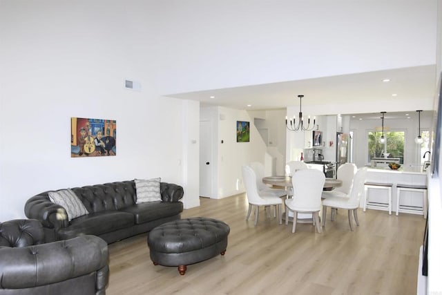 living room with a notable chandelier, light hardwood / wood-style flooring, and a high ceiling