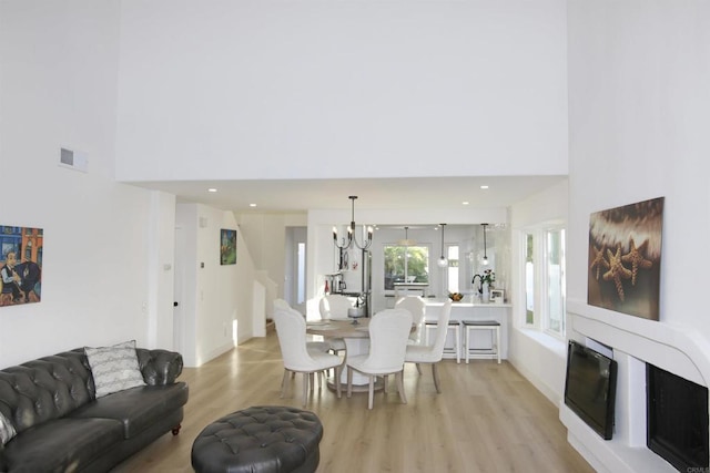 living room featuring a towering ceiling, a chandelier, and light wood-type flooring