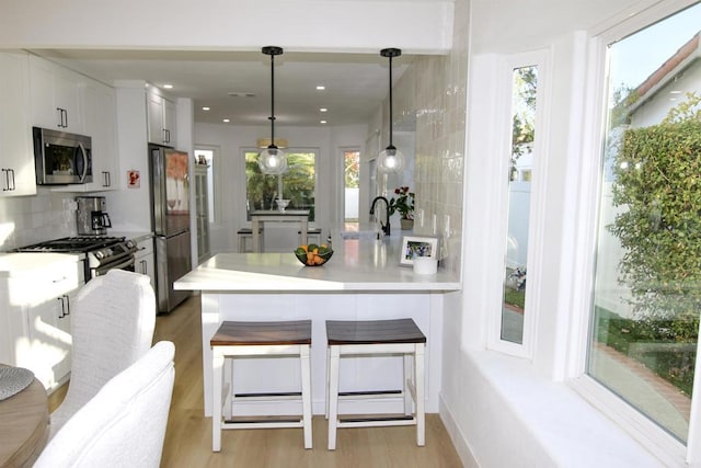 kitchen with appliances with stainless steel finishes, white cabinetry, a wealth of natural light, decorative light fixtures, and kitchen peninsula