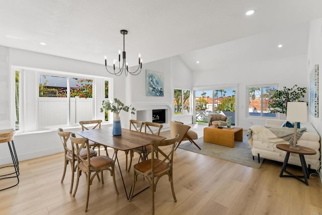 dining area featuring lofted ceiling, light wood-style flooring, a fireplace, a chandelier, and recessed lighting