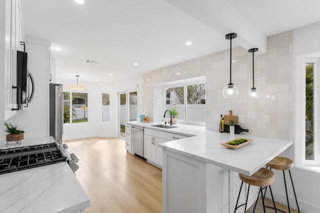 kitchen featuring white cabinets, light stone countertops, stainless steel appliances, light wood-type flooring, and a sink