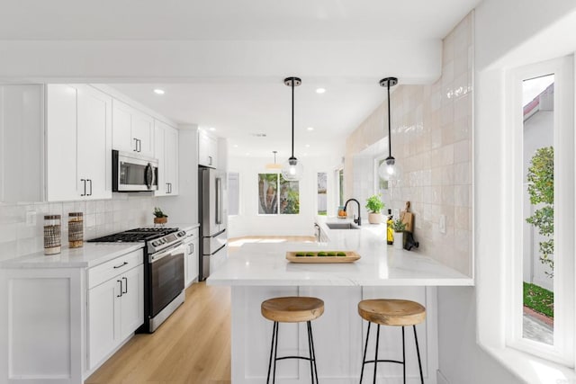 kitchen featuring decorative backsplash, a breakfast bar, a peninsula, stainless steel appliances, and a sink