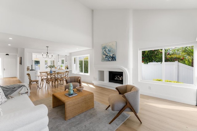 living area with a fireplace with raised hearth, recessed lighting, a towering ceiling, and light wood-style floors