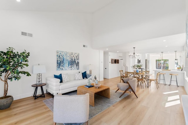 living room with light wood finished floors, visible vents, a towering ceiling, a chandelier, and recessed lighting