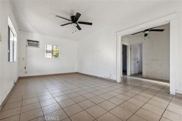 spare room featuring light tile patterned floors, a wall unit AC, and ceiling fan