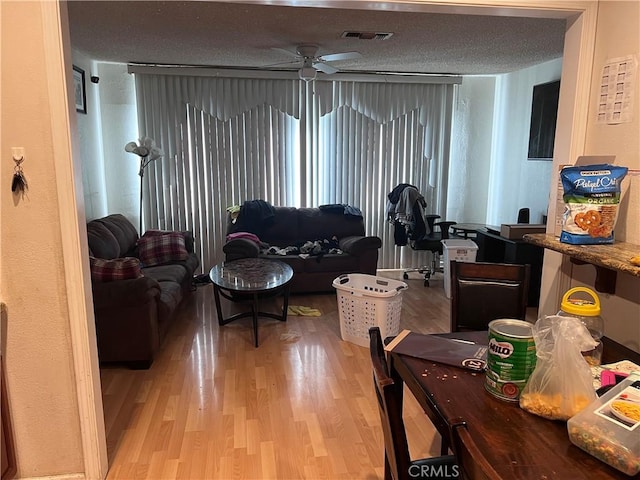 living room with ceiling fan, light wood-type flooring, and a textured ceiling