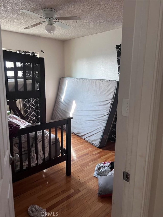 bedroom with ceiling fan, a textured ceiling, and hardwood / wood-style flooring