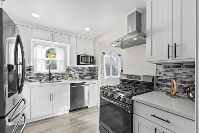 kitchen with stainless steel appliances, white cabinetry, a wealth of natural light, and wall chimney range hood