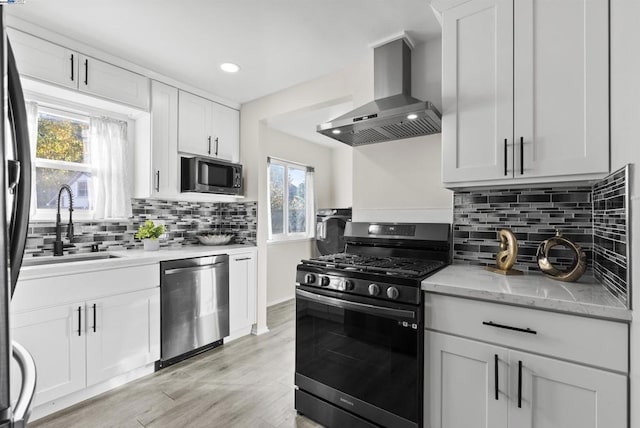 kitchen with white cabinets, wall chimney exhaust hood, light wood-type flooring, and stainless steel appliances