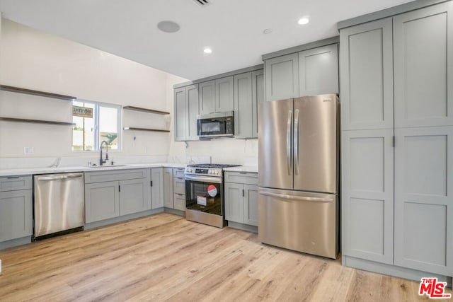 kitchen with gray cabinets, stainless steel appliances, light hardwood / wood-style flooring, and sink