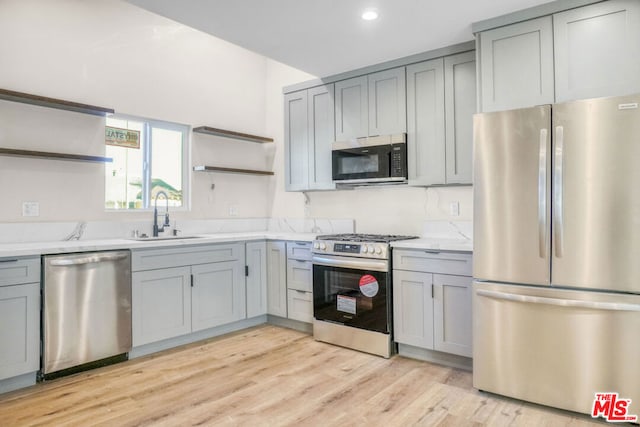 kitchen featuring gray cabinetry, sink, light wood-type flooring, light stone counters, and stainless steel appliances