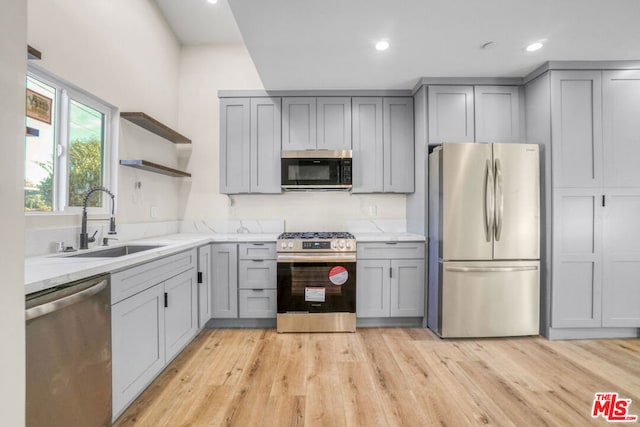 kitchen with gray cabinets, stainless steel appliances, light hardwood / wood-style flooring, and sink