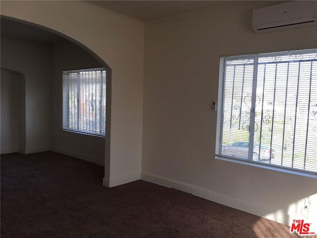 empty room with dark colored carpet, a wall unit AC, and a wealth of natural light