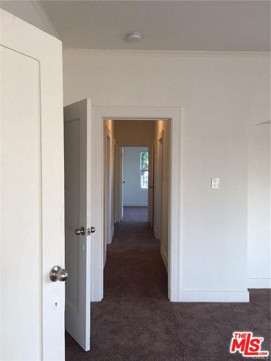 corridor featuring dark carpet and crown molding