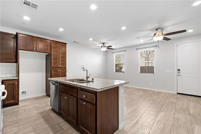 kitchen featuring a center island with sink, sink, stainless steel dishwasher, ceiling fan, and light stone countertops