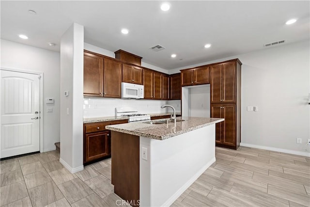 kitchen featuring white appliances, a center island with sink, light stone counters, and sink