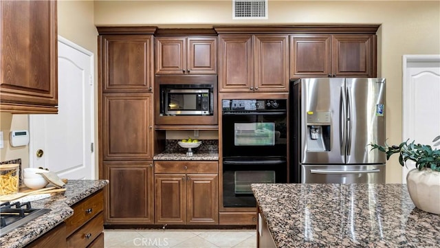 kitchen featuring stainless steel appliances, dark stone countertops, and light tile patterned flooring