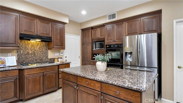 kitchen featuring backsplash, stainless steel appliances, light tile patterned floors, dark stone countertops, and a kitchen island