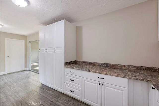 kitchen featuring white cabinets, a textured ceiling, light hardwood / wood-style flooring, and dark stone counters