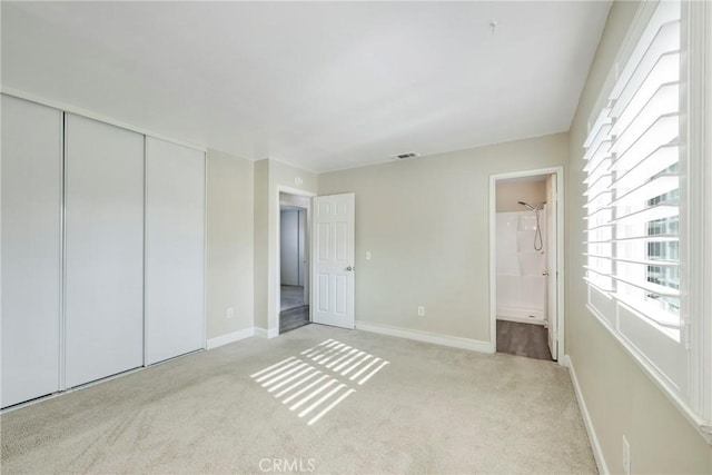 unfurnished bedroom featuring ensuite bathroom, light carpet, and a closet