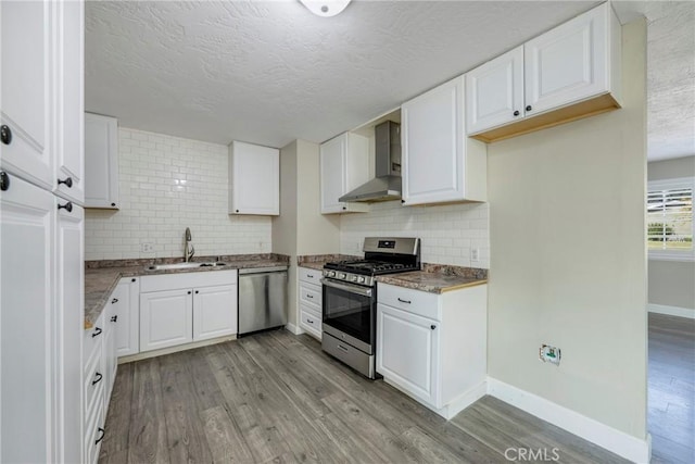 kitchen featuring white cabinetry, sink, stainless steel appliances, wall chimney range hood, and light hardwood / wood-style floors