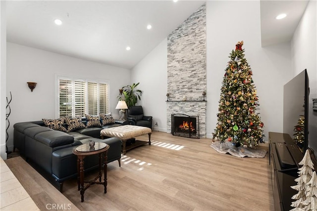 living room featuring a stone fireplace, high vaulted ceiling, and light hardwood / wood-style flooring