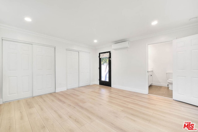 unfurnished bedroom featuring connected bathroom, multiple closets, a wall mounted air conditioner, crown molding, and light hardwood / wood-style floors