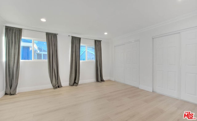 unfurnished bedroom with light wood-type flooring, two closets, and multiple windows