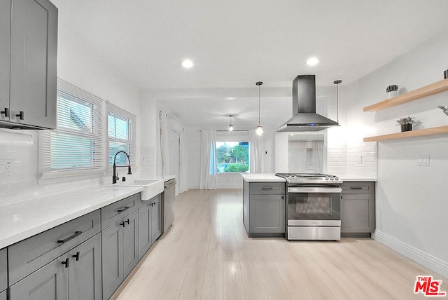 kitchen with gray cabinetry, light hardwood / wood-style flooring, wall chimney exhaust hood, decorative light fixtures, and stainless steel appliances