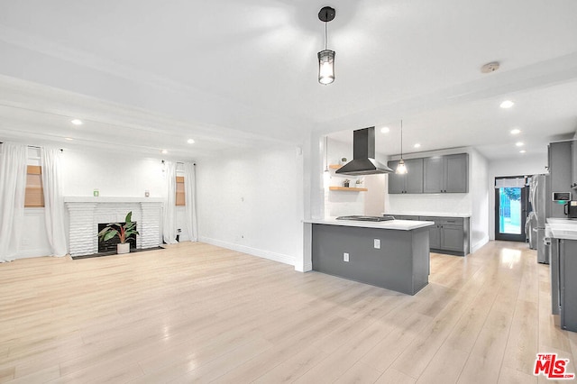 kitchen with pendant lighting, light hardwood / wood-style floors, range hood, and a brick fireplace