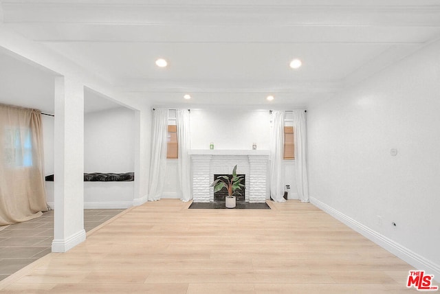 living room featuring beamed ceiling, light wood-type flooring, and a fireplace