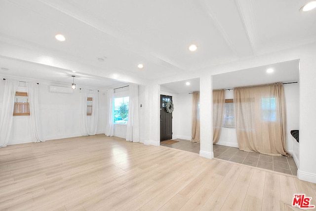 unfurnished room with beam ceiling, light wood-type flooring, and a wall unit AC