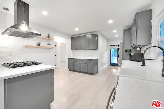 kitchen with pendant lighting, stainless steel gas stovetop, gray cabinets, light wood-type flooring, and island range hood