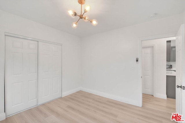 unfurnished bedroom featuring an inviting chandelier, light hardwood / wood-style flooring, and a closet