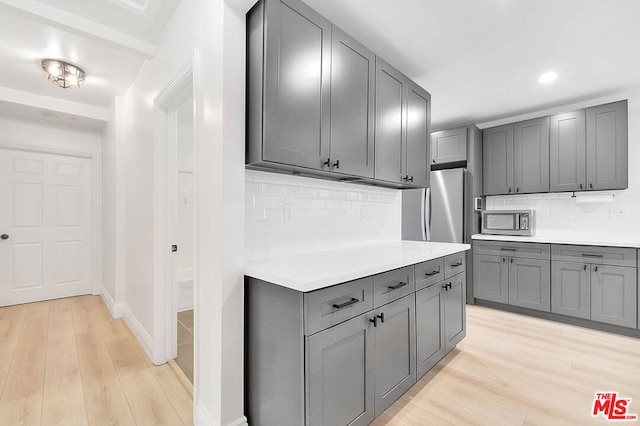 kitchen featuring decorative backsplash, appliances with stainless steel finishes, light hardwood / wood-style floors, and gray cabinetry