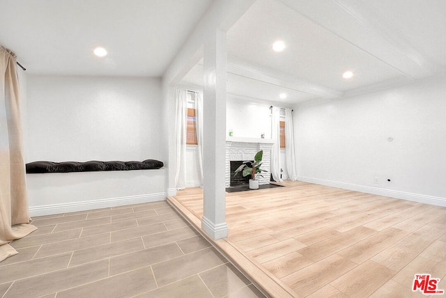 interior space with beamed ceiling, a brick fireplace, and light hardwood / wood-style flooring