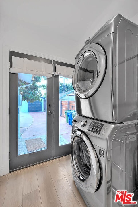 clothes washing area featuring french doors, light hardwood / wood-style flooring, and stacked washer / drying machine