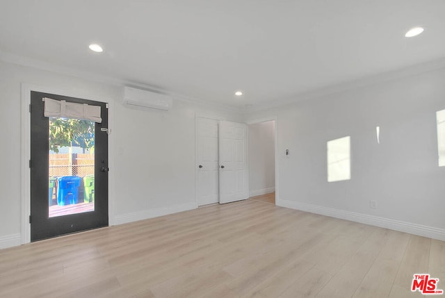 empty room featuring light wood-type flooring, crown molding, and a wall mounted AC