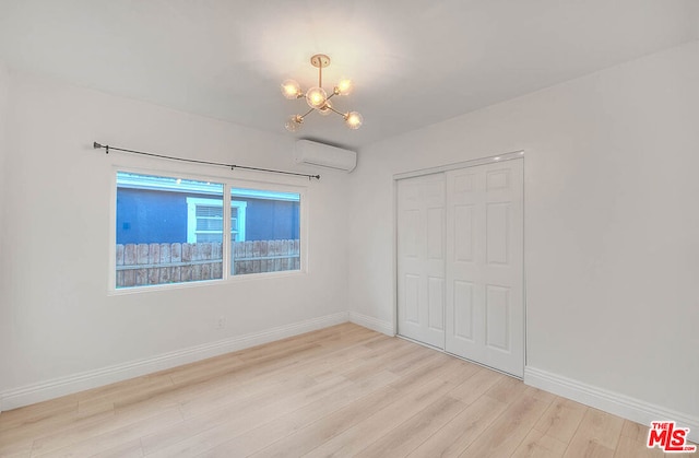 unfurnished bedroom featuring a chandelier, light wood-type flooring, a closet, and a wall mounted AC