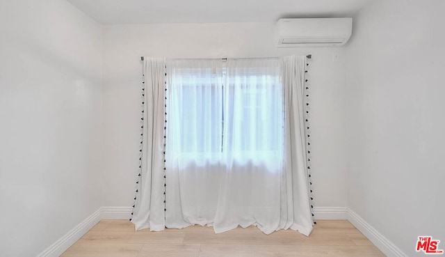 empty room featuring a wall mounted air conditioner and light wood-type flooring