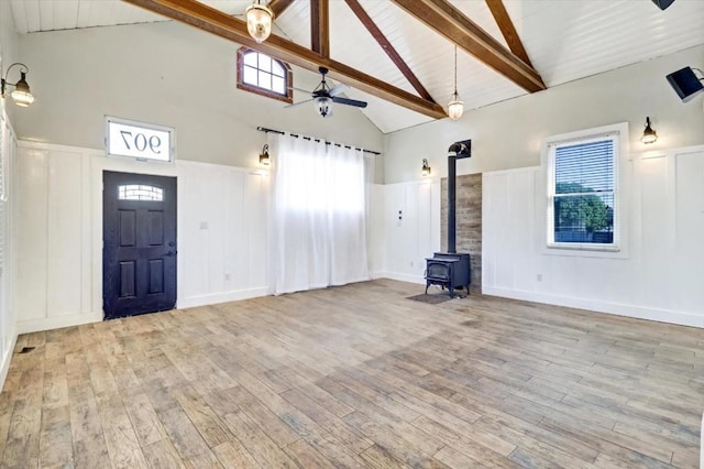 unfurnished living room with a wood stove, high vaulted ceiling, ceiling fan, beamed ceiling, and light hardwood / wood-style floors