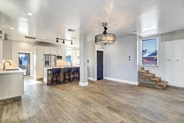 kitchen with sink, appliances with stainless steel finishes, decorative backsplash, white cabinets, and light wood-type flooring