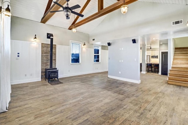 unfurnished living room with beam ceiling, wood-type flooring, a wood stove, and high vaulted ceiling