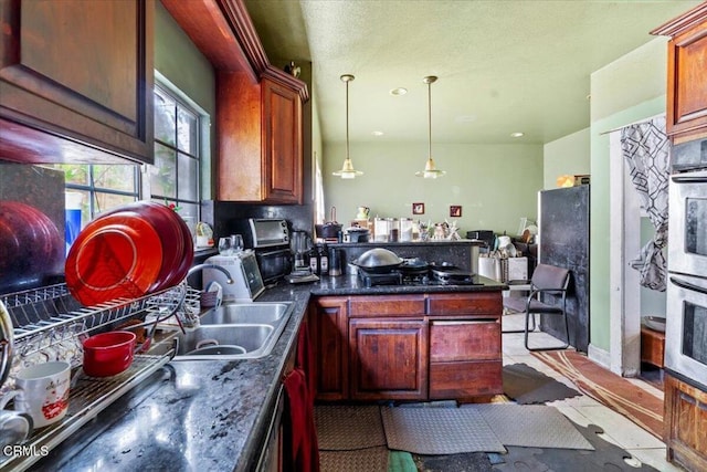 kitchen featuring sink, double oven, black gas stovetop, dark stone counters, and decorative light fixtures